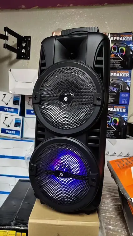 Bocina con luces LED encendidas sobre el mostrador de TecnoCity SV, con cajas de producto en los estantes del fondo