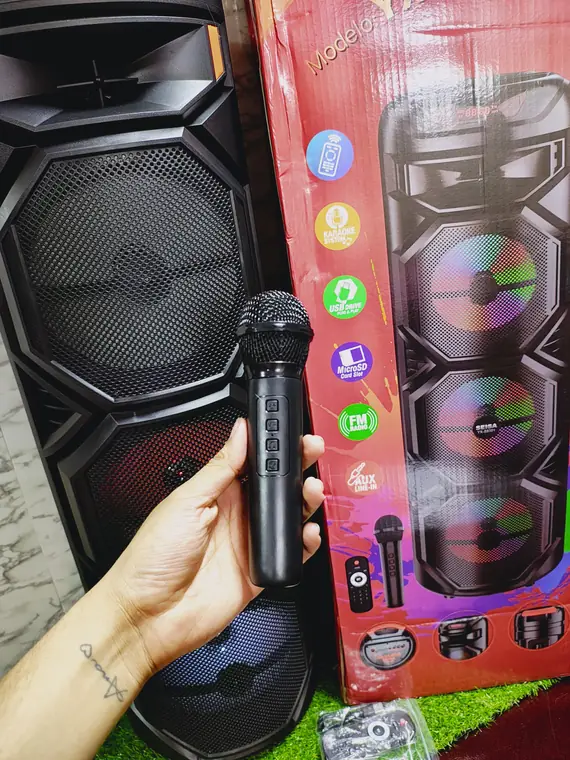 Micrófono de karaoke en mano frente a bocinas con luces de colores